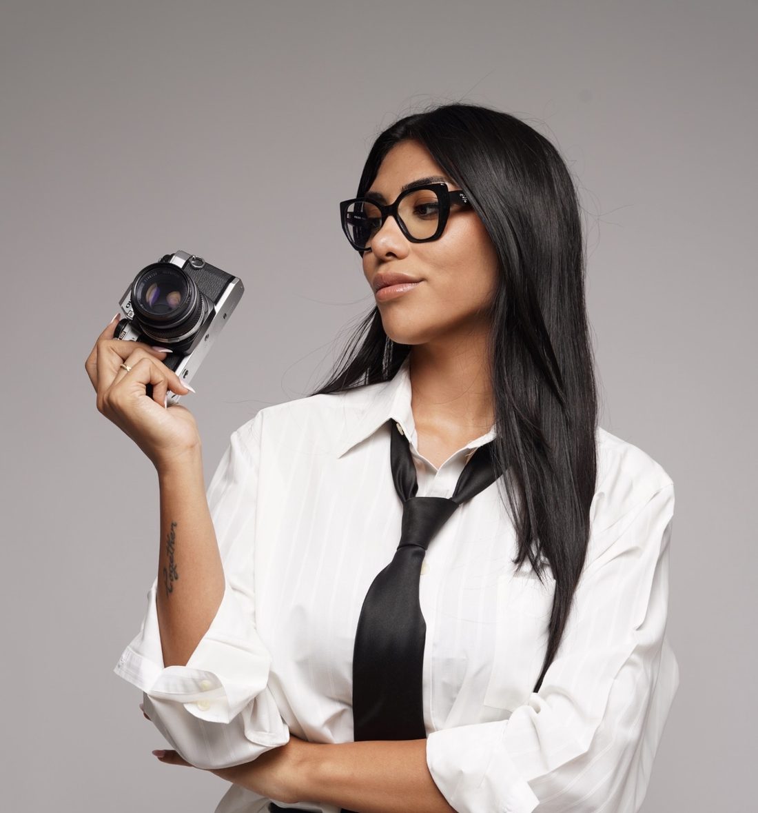 Irina Luna, founder of Moon Social Lab, holding a vintage film camera in a white shirt and black tie