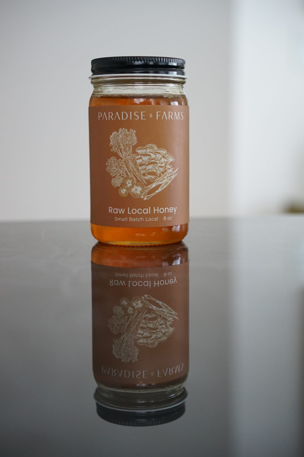 Jar of raw local honey from Paradise Farms with its reflection on a dark surface