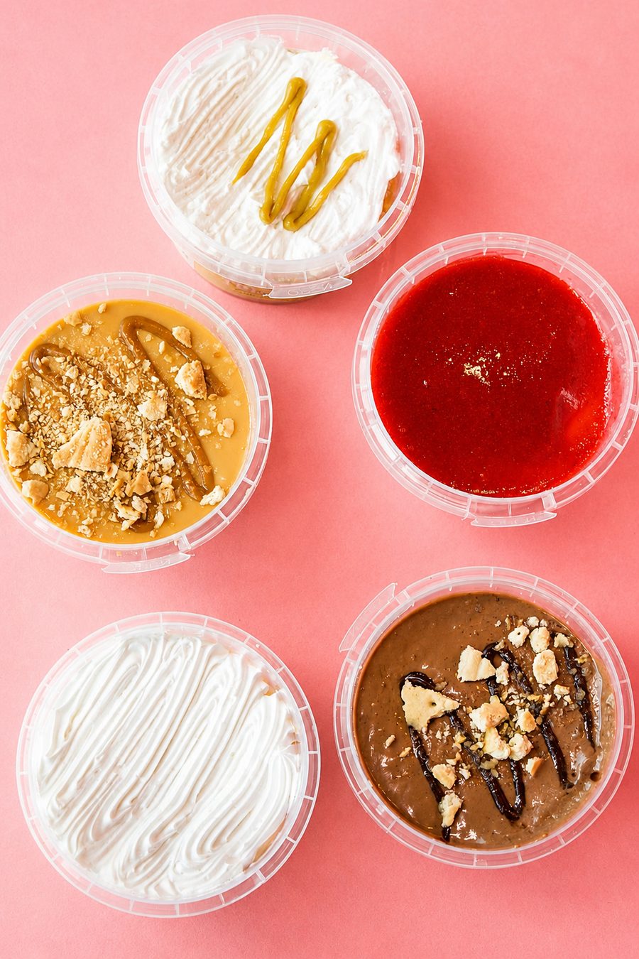 Overhead shot of five dessert cups with different toppings on a coral pink background